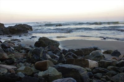 Rocks on beach against sky during sunset