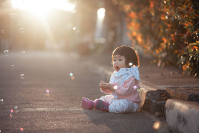 Cute girl looking at bubbles while sitting on road