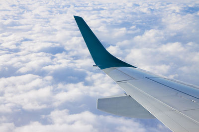 Cropped image of airplane wing flying over cloudy sky