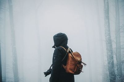 Rear view of person with backpack standing at forest during foggy weather