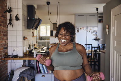 Joyful mature woman dancing and exercising with dumbbells at home