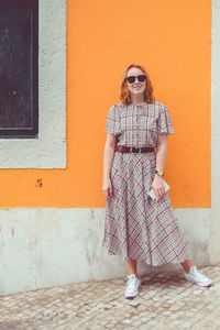 Young woman wearing sunglasses standing against built structure