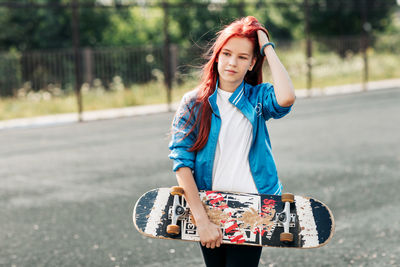 Portrait of a charming girl with a skateboard in her hand on a sports field