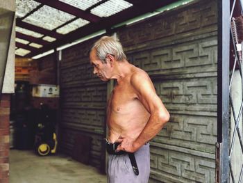 Side view of shirtless man standing against wall