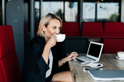 A young woman is drinking coffee in a cafe during a break and working at a laptop. business concept
