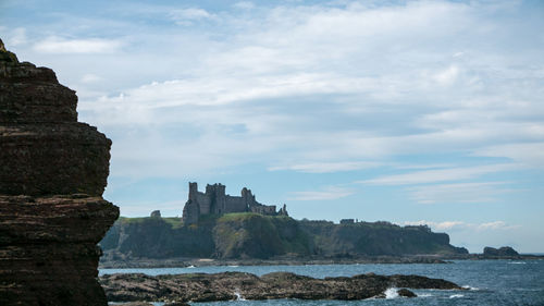 Buildings by sea against cloudy sky