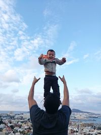 Rear view of playful father throwing son in air against sky