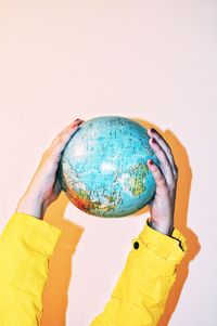 Cropped hands holding globe against wall