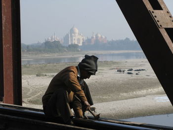 Man sitting at temple against sky in city