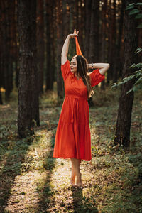 Alone woman in red dress dance on sun pine forest nature background