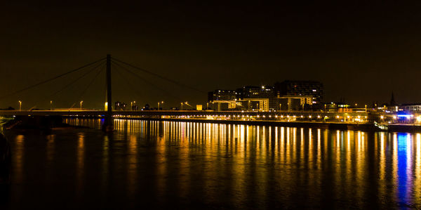 Illuminated bridge over river against sky at night