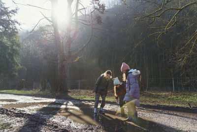 Rear view of friends playing with puddles on the country road in forest