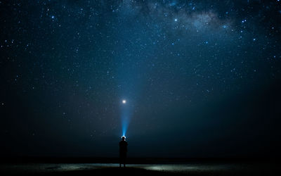 Rear view of man flashing light in sky at night