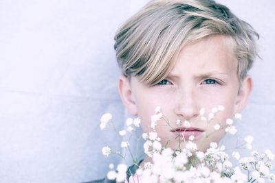 Close-up portrait of cute girl against white flowering plant