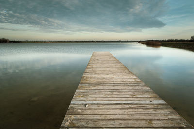 Long wooden bridge on the lake, evening clouds on the sky