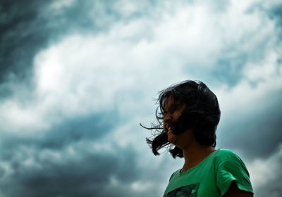 Low angle view of teenage girl with tousled hair standing against cloudy sky