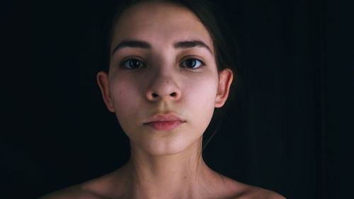 Close-up portrait of young woman against black background