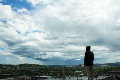 Rear view of man standing by cityscape against sky