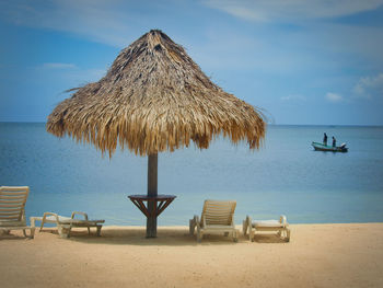 Lounge chairs palapa, and parasols on beach against sky