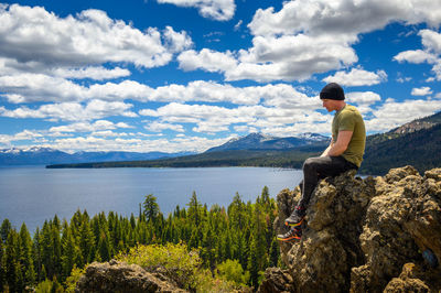 Rear view of man standing on rock by lake against sky