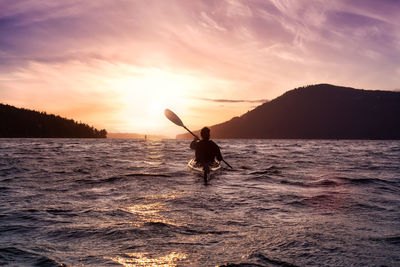 Silhouette man in sea against sky during sunset