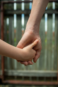 Cropped image of people holding hands against railing