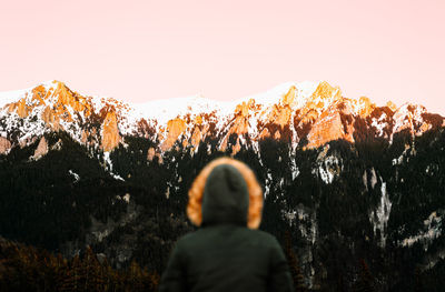 Rear view of person looking at snowcapped mountains against clear sky at sunset