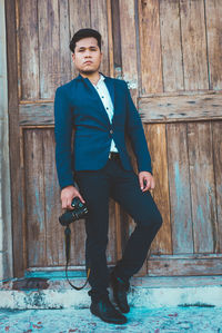 Portrait of young man standing against wooden wall