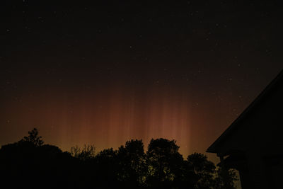 Red and yellow ribbons of light from aurora borealis against stars and silhouette trees and roof
