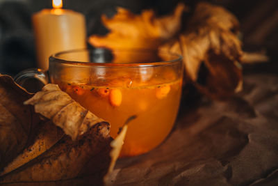 Burning candle and a large mug of hot orange sea buckthorn tea in a cozy home autumn 