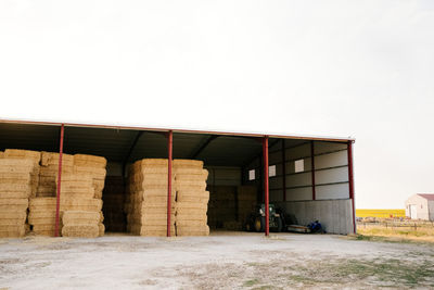 Industrial shelter with stacked hay rolls in remote agricultural fields of sunny countryside