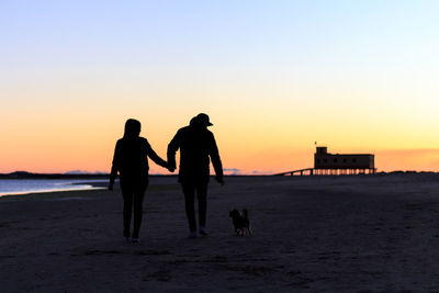 Silhouette couple with dog walking on beach at sunset