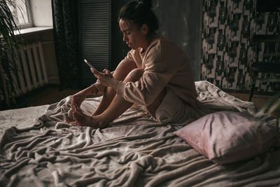 Woman using mobile phone while sitting on bed at home