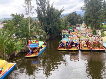 Multi colored boats in river by trees against sky