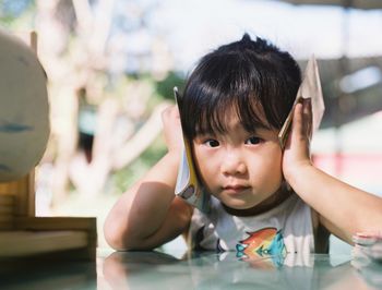 Portrait of cute girl closing ears with hands while sitting by table