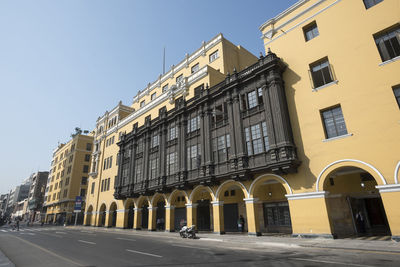 Road by buildings against clear sky in city