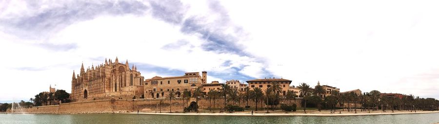 Buildings by river against cloudy sky