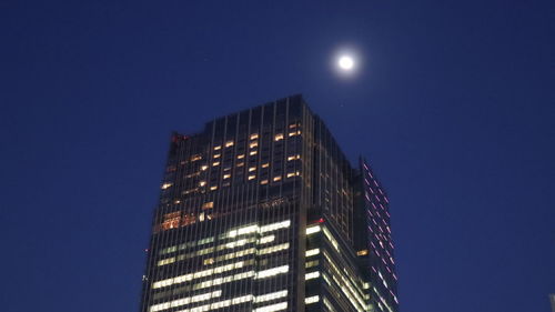 Low angle view of illuminated skyscraper against blue sky