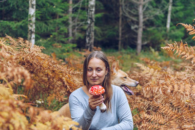 Woman holding mushroom while sitting by dog in forest