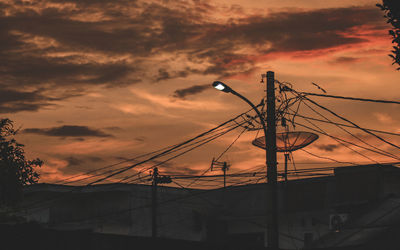 Low angle view of silhouette power lines against orange sky