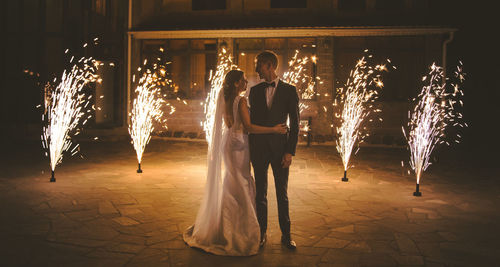 Bride and bridegroom standing against firework at night