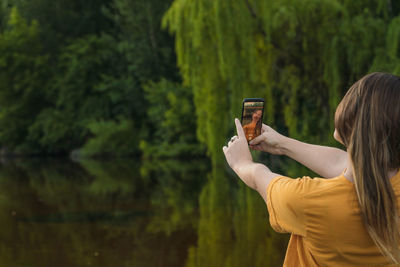 Rear view of woman doing selfie against trees