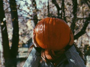 Teenage girl covering face with pumpkin
