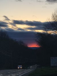 Cars on street against sky at sunset