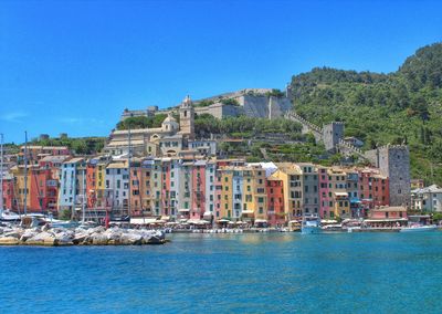 Buildings by sea against clear blue sky