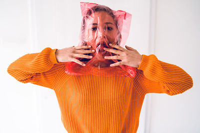 Portrait of teenage girl face covered with plastic bag standing against wall at home