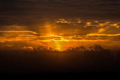 Silhouette landscape against dramatic sky during sunset