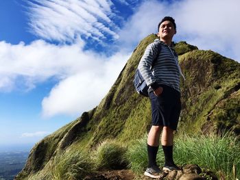 Young man looking away while standing on mountain against cloudy sky