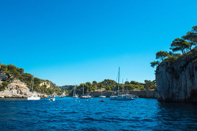 Boats moored on sea against clear blue sky