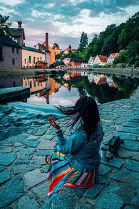 Rear view of woman sitting in swimming pool against buildings